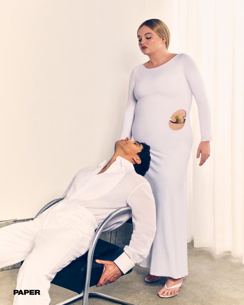 Megan Stalter in a white cutout dress standing beside Paul W. Downs reclining in a chair in all white for Paper Magazine.