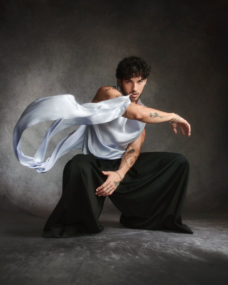 Luis Capecchi crouching in wide-leg black trousers with flowing satin fabric in an editorial shoot for Numéro Homme Switzerland.