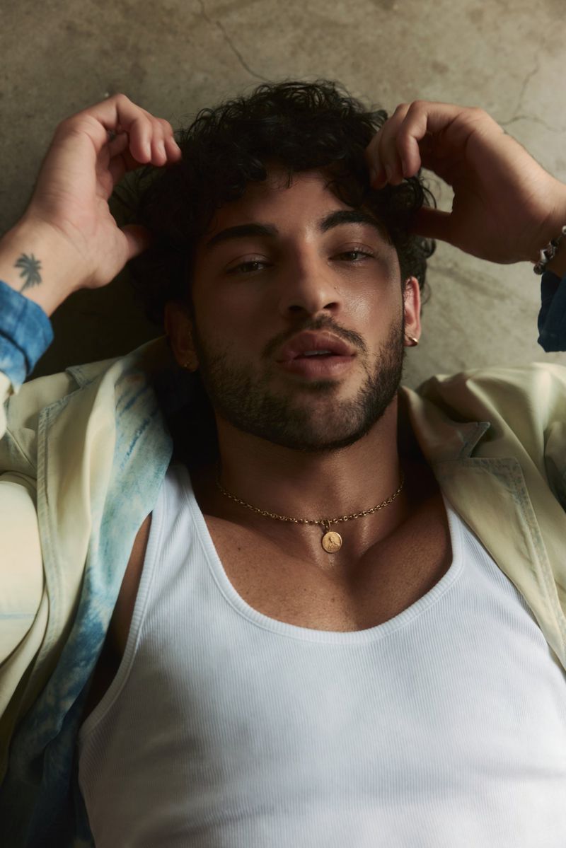 Luis Capecchi lying down wearing a white ribbed tank top and gold pendant necklace for Numéro Homme Switzerland.