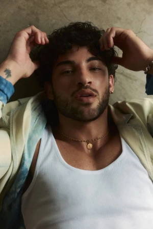 Luis Capecchi lying down wearing a white ribbed tank top and gold pendant necklace for Numéro Homme Switzerland.