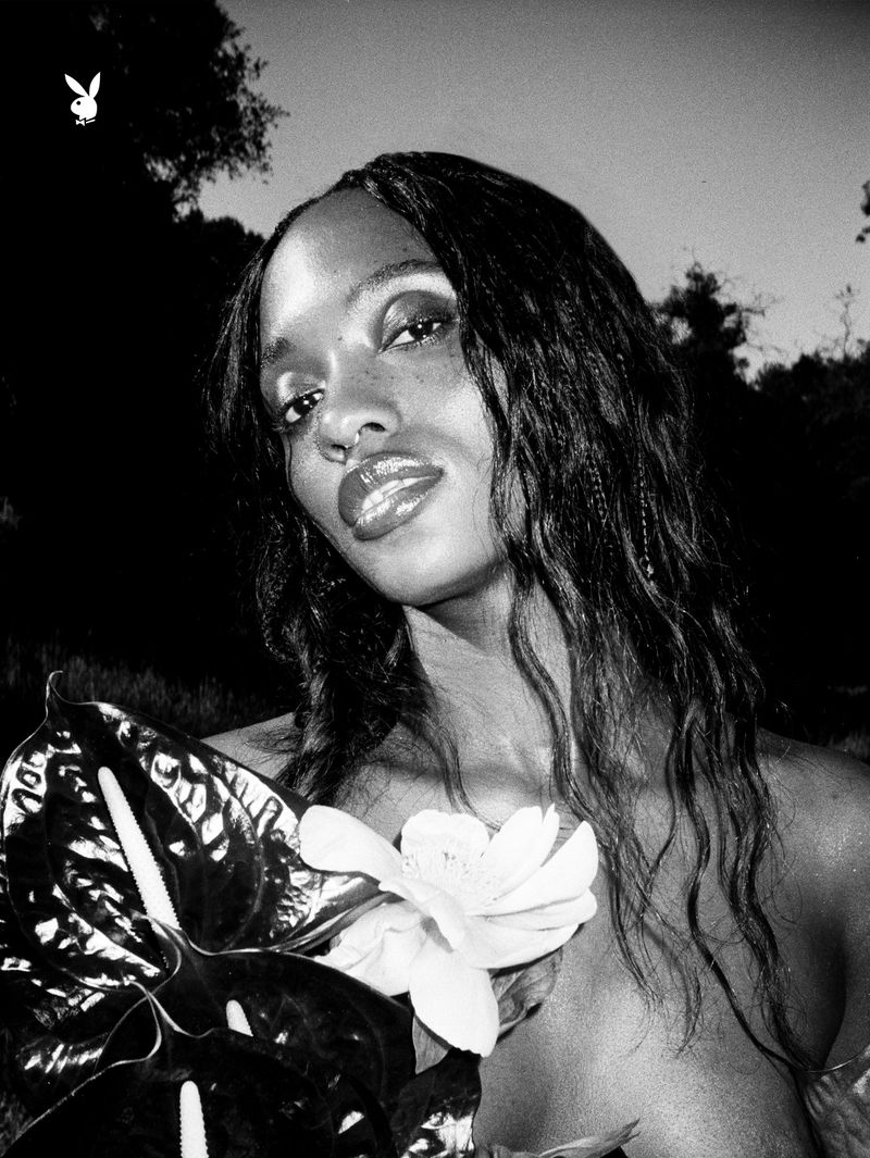 Black and white portrait of Gabrielle Richardson holding anthurium and magnolia blossoms outdoors with the Playboy logo in the corner.