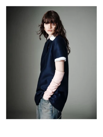 Model wearing a navy blue collared polo shirt with pale pink arm warmers and denim jeans against a grey studio backdrop.