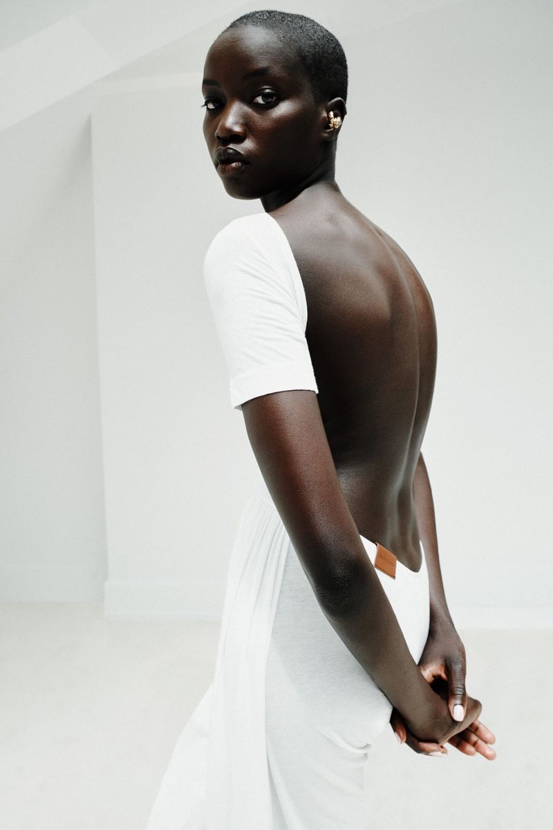Anok Yai wearing an open-back white short-sleeved top looking over her shoulder against a minimalist white backdrop.
