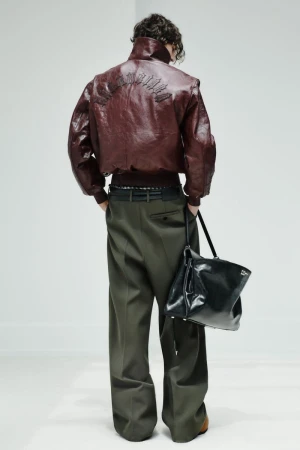 Model seen from behind wearing a burgundy leather bomber jacket, olive wide-leg trousers, and holding a glossy black leather bag.
