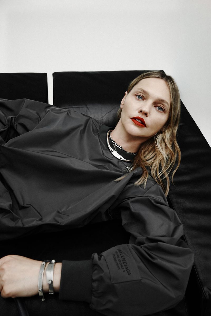 Model lying on dark surface wearing a dark grey sweatshirt with red lips against a neutral background
