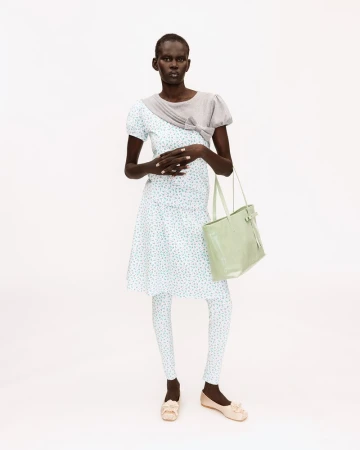 Black female model posing in a blue floral dress, matching printed leggings, grey shrug, and light green tote on a white background.