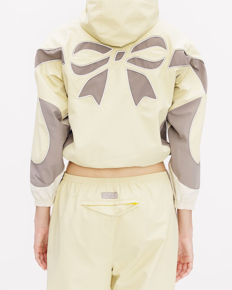 Model from behind wearing a pale yellow hooded jacket with a large bow design and matching pants against a white background.