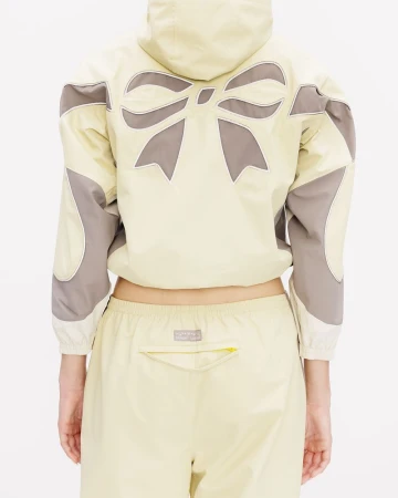 Model from behind wearing a pale yellow hooded jacket with a large bow design and matching pants against a white background.