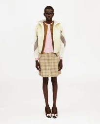 Model wearing a light hooded jacket, pink cardigan, beige plaid mini skirt, and bow flats against a white seamless background.