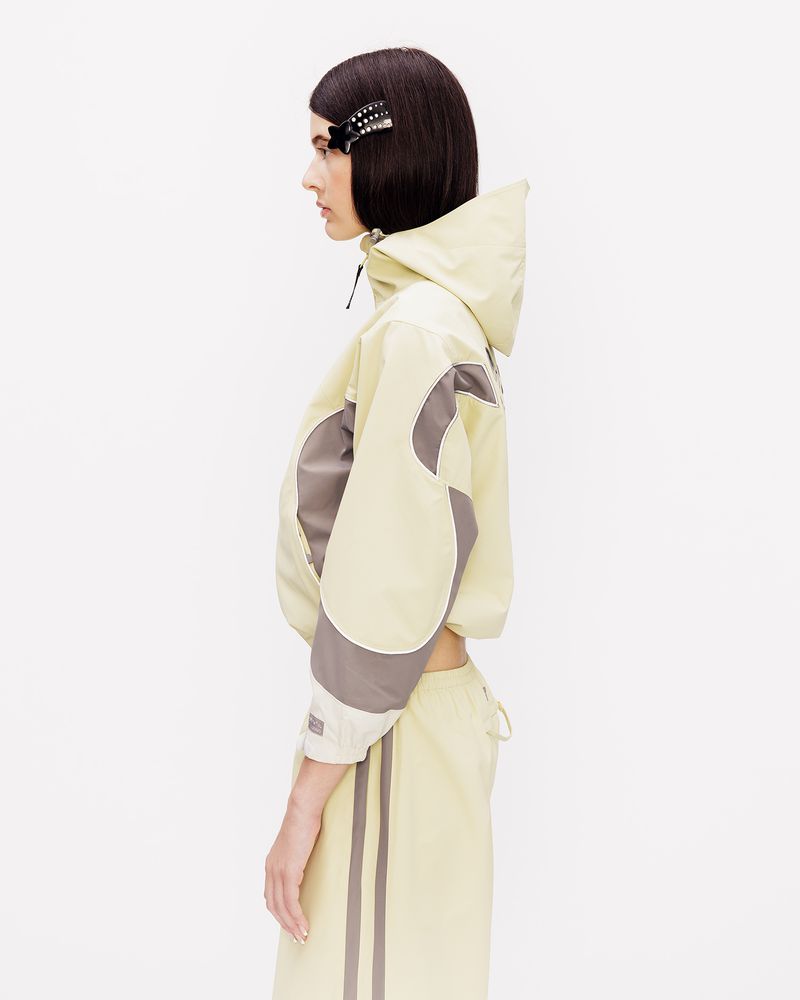 Model in profile wearing a pale yellow hooded jacket and matching bottoms with grey accents against a white background.