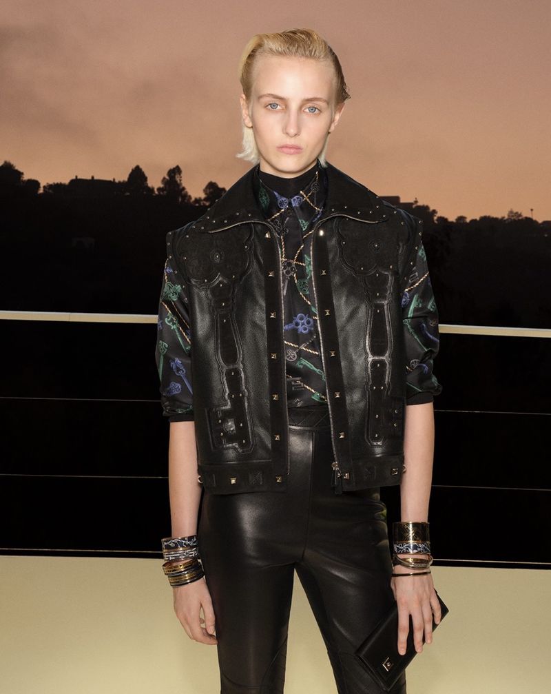 Model with short blonde hair wearing a black studded leather vest and black leather pants at sunset.