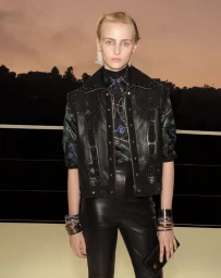 Model with short blonde hair wearing a black studded leather vest and black leather pants at sunset.