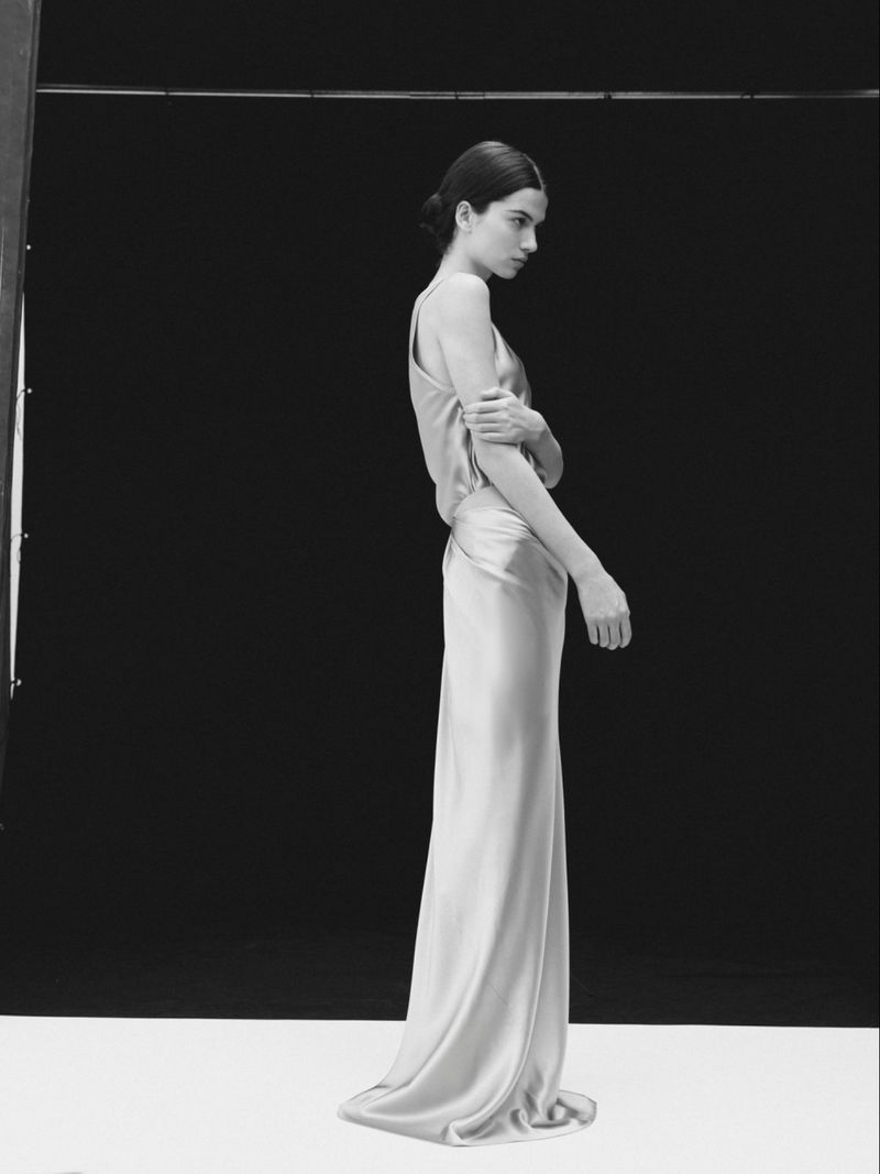 Model Peyton Cole wearing a long draped satin gown in a studio setting against a black backdrop.