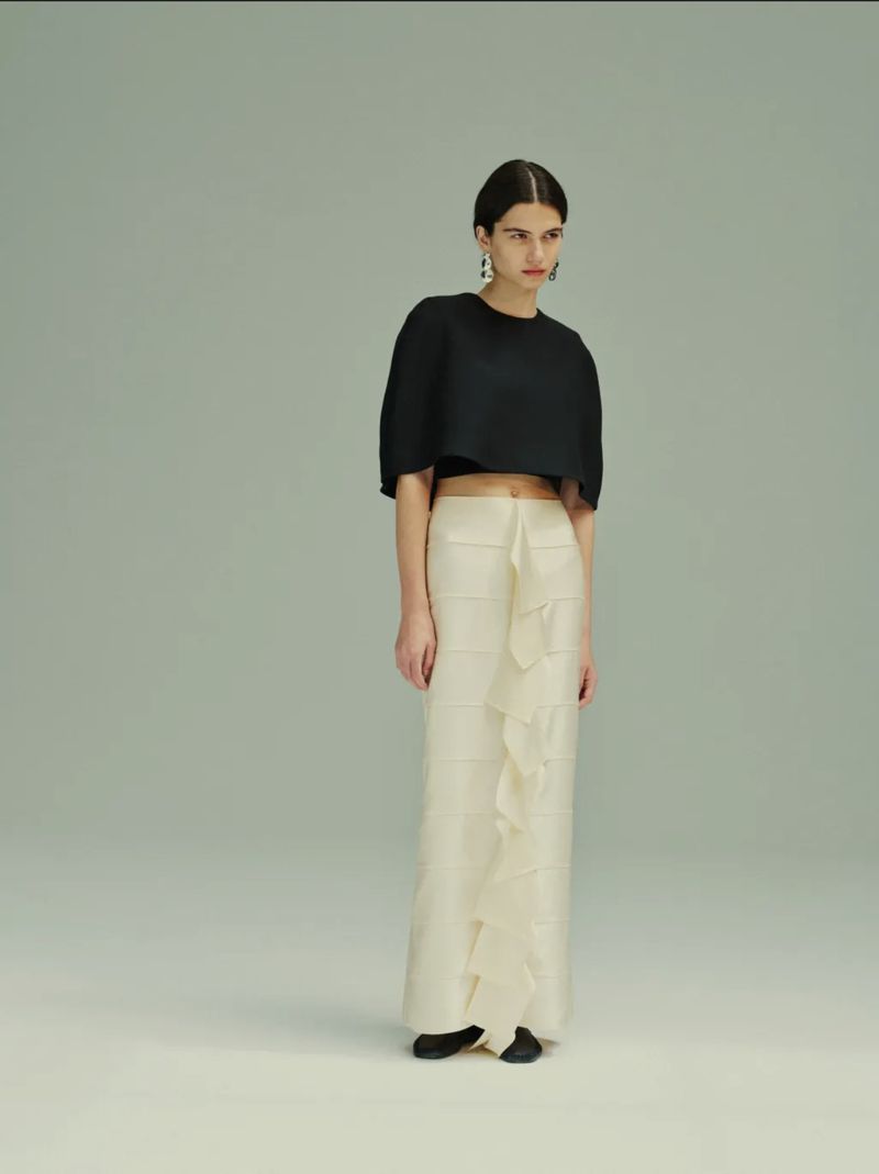 Model Peyton Cole wearing a black cropped top and cream tiered ruffle maxi skirt against a pale studio backdrop.