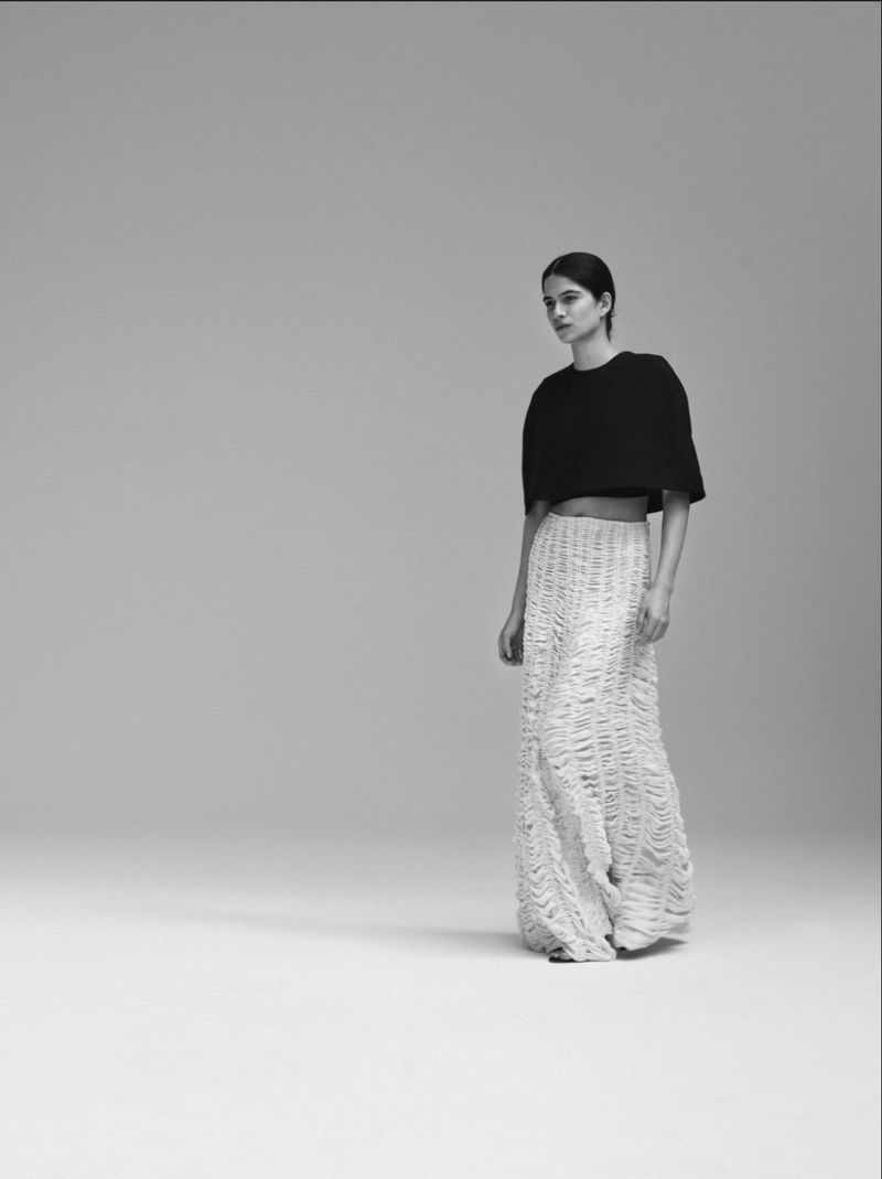 Model Peyton Cole wearing a black cropped short-sleeve top and textured white maxi skirt against a seamless studio backdrop.