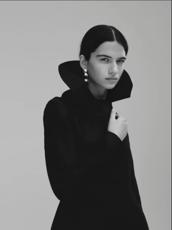 Model Peyton Cole in a high structured collar black coat with a metallic drop earring against a neutral backdrop.
