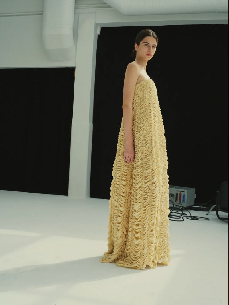 Model Peyton Cole wearing a full-length strapless textured pale yellow gown on a white studio floor in front of a dark backdrop.