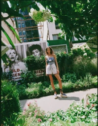 Model standing outdoors in a garden wearing patterned shorts and a strappy top for Loeffler Randall Spring 2026 Lookbook