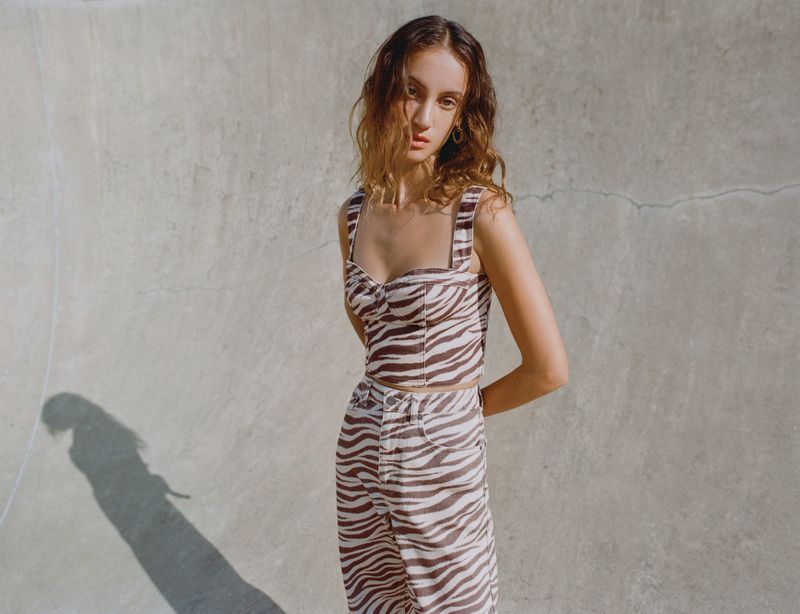 Model Sam Nixon posing in a brown and white zebra print corset top and matching trousers against a curved concrete wall.