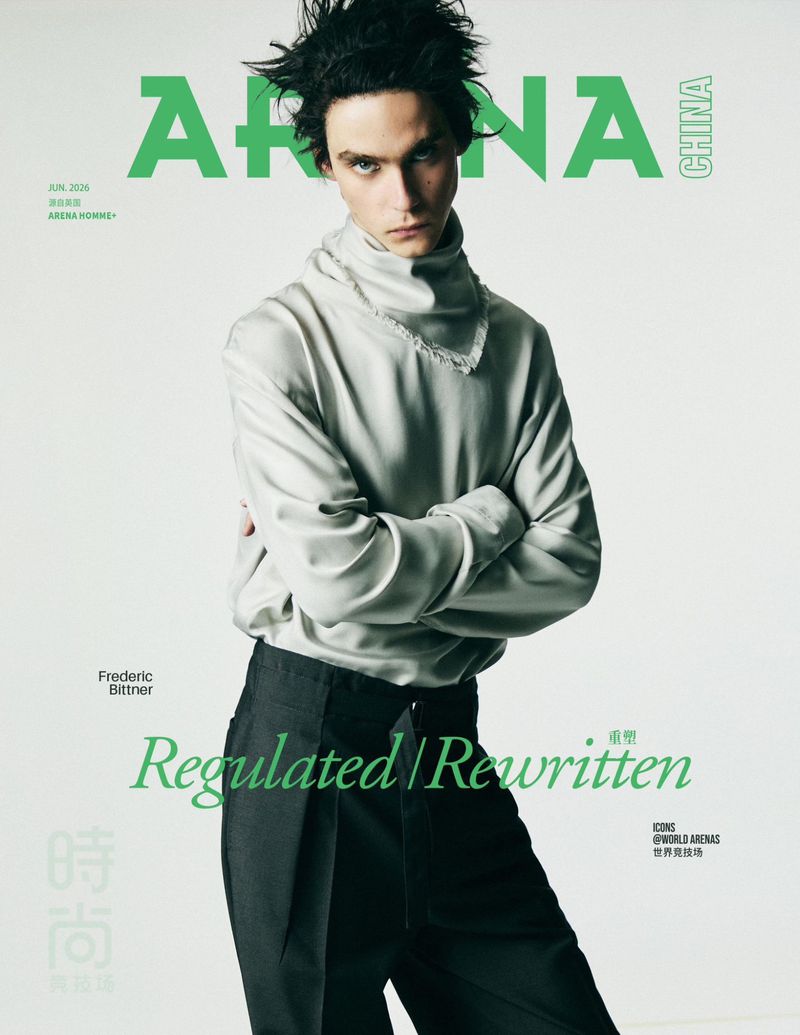 Model Frederic Bittner posing with arms crossed in a high-neck grey top and tailored black trousers on a white backdrop.