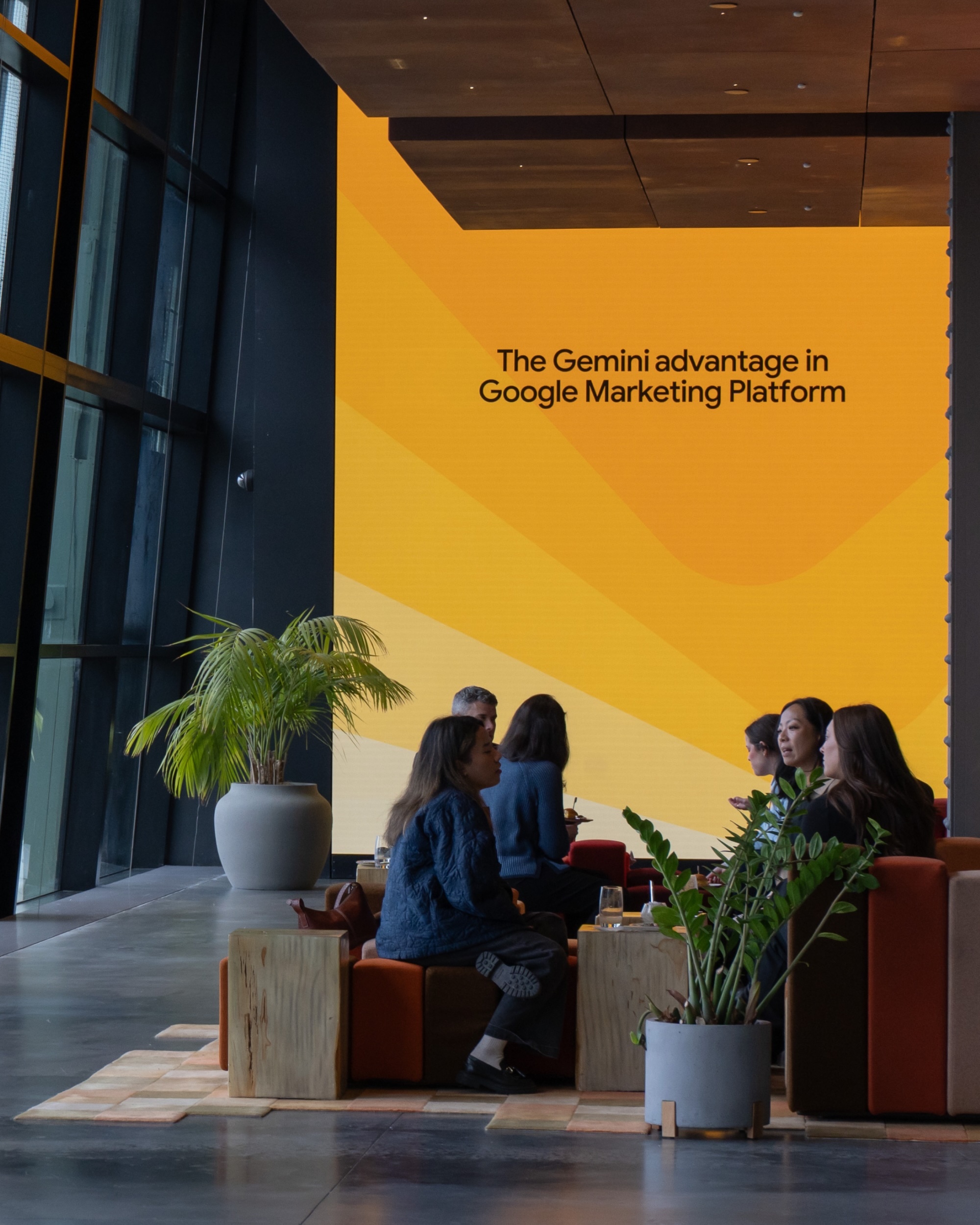 People seated in a lounge area in front of a large yellow screen displaying The Gemini advantage in Google Marketing Platform.