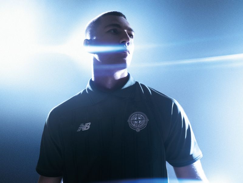 Man in a dark green Stone Island and New Balance collared shirt illuminated by bright blue horizontal backlight flares.