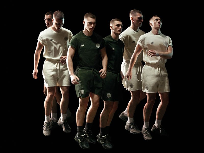 Six male models walking forward in matching cream and dark green t-shirt and short sets against a solid black background.