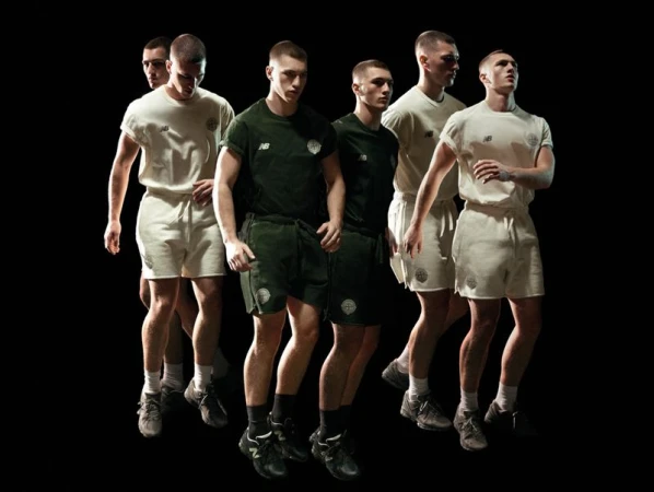 Six male models walking forward in matching cream and dark green t-shirt and short sets against a solid black background.
