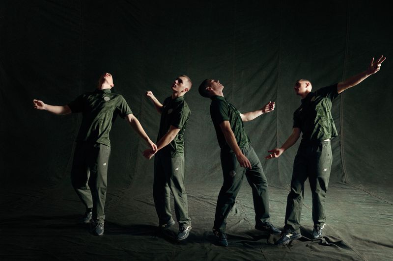 Four male figures in matching dark olive green sportswear posing dynamically against a dark textured backdrop.