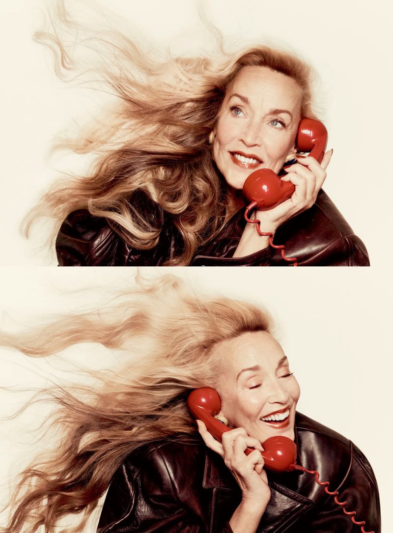 Jerry Hall holding a red telephone receiver and wearing a black leather jacket against an off-white background.