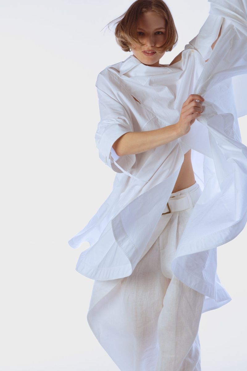 Model in a flowing white shirt and matching trousers against a plain white studio background.