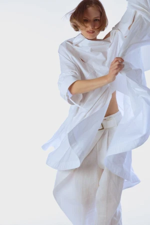 Model in a flowing white shirt and matching trousers against a plain white studio background.