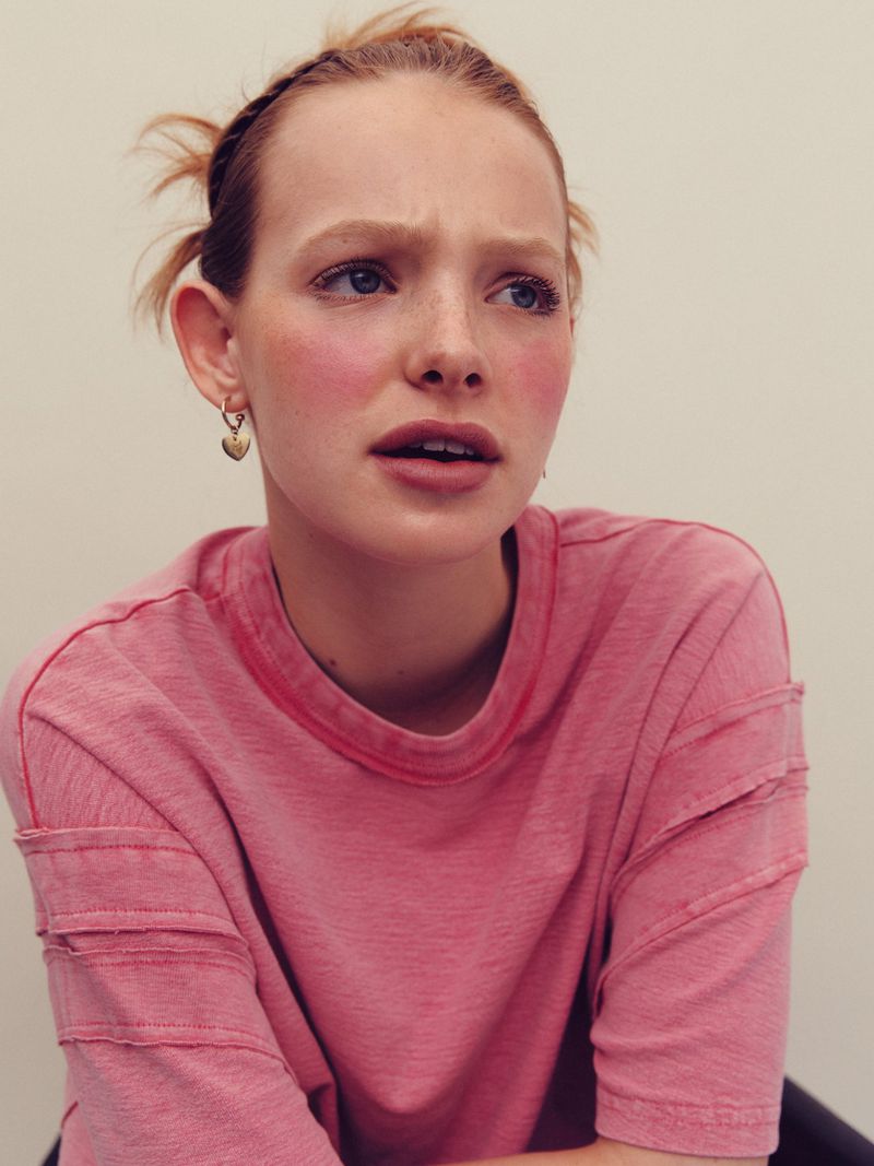 Close-up portrait of a woman with red hair wearing a pink t-shirt against a plain neutral background