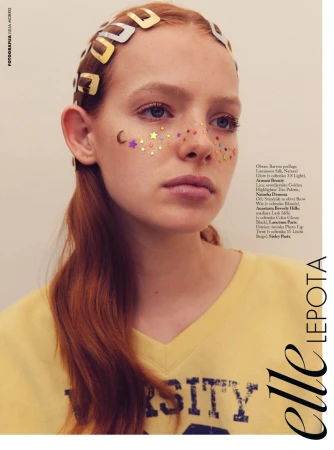 Beauty editorial portrait of a woman with red hair, metallic hair clips along her hairline, and celestial face glitter across her cheeks and nose.