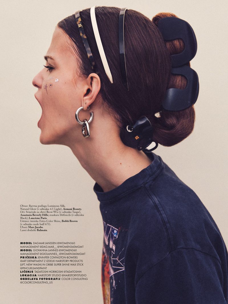 Profile of a woman shouting, wearing multiple headbands and oversized black hair clips in an updo against a beige backdrop.