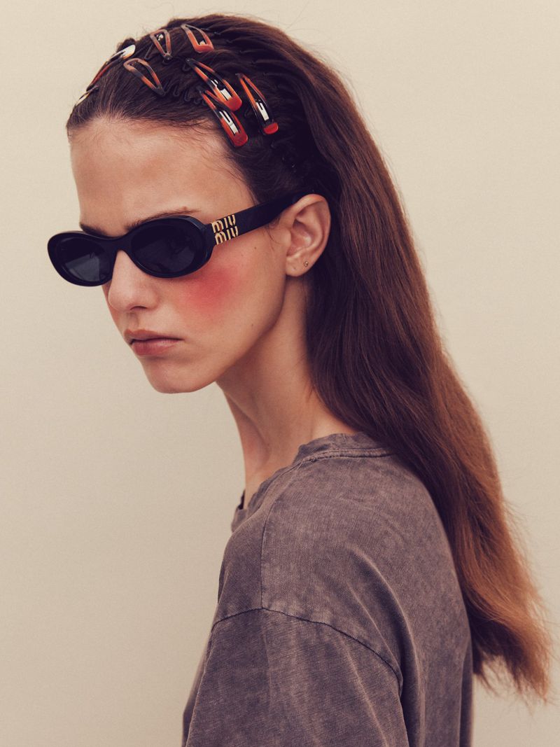 Model wearing black oval sunglasses and multiple tortoise hair clips in long brown hair against a neutral studio backdrop.