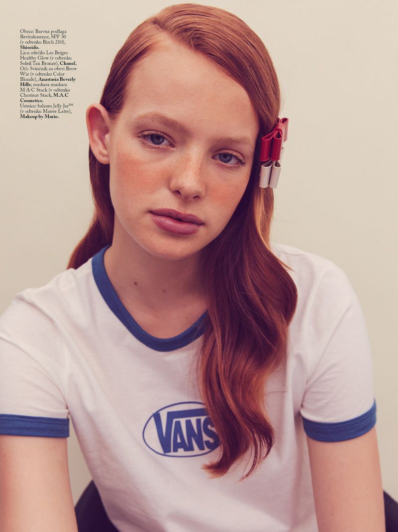 Redheaded woman in a white and blue Vans ringer t-shirt wearing red and white ribbons in her auburn hair against an off-white background.