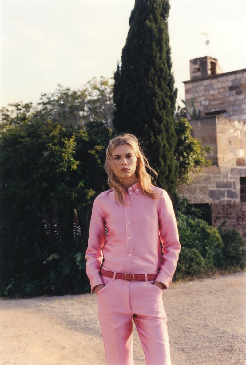 Model Freya Nutter posing outdoors in a pastel pink button-down shirt and matching trousers with a slim belt.