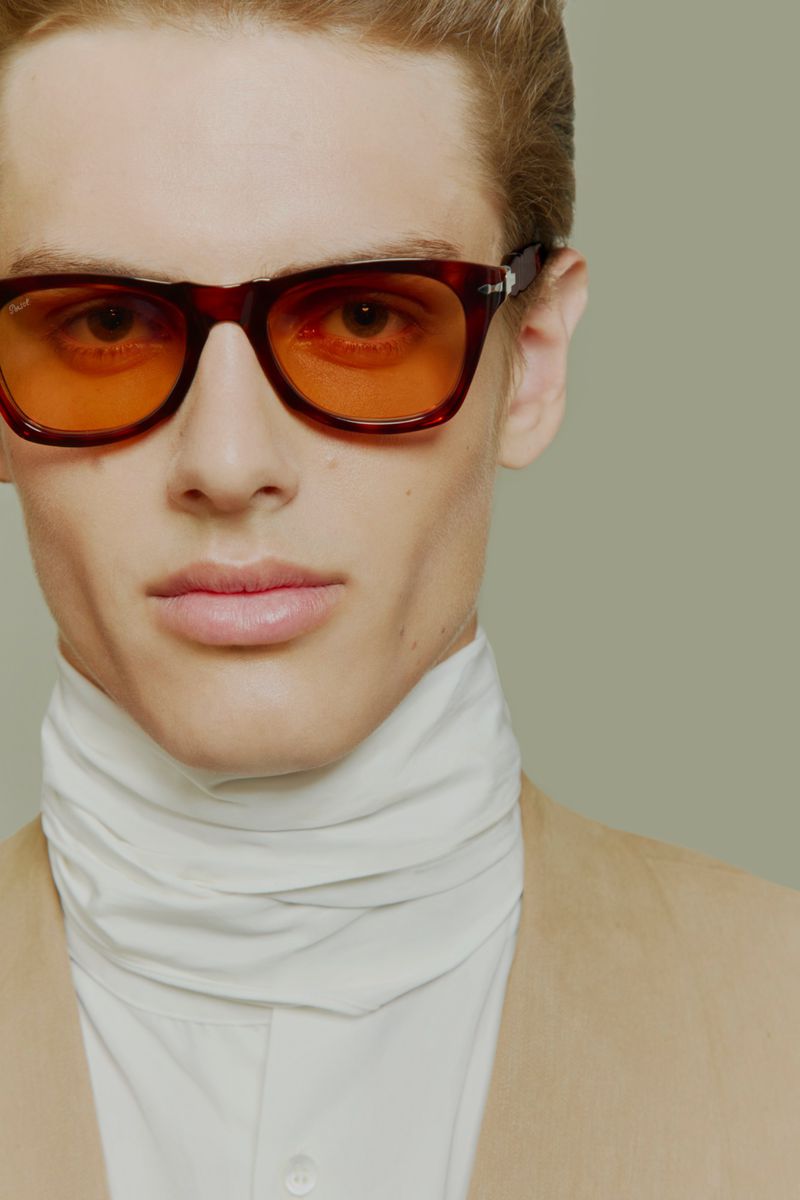 Esteban Monbaliu wearing tortoiseshell sunglasses with orange tinted lenses and a high white collar against a studio background.