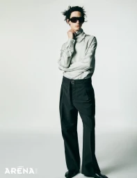Model Frederic Bittner posing in black sunglasses, a draped off-white high-neck shirt, and black wide-leg trousers on a white backdrop.