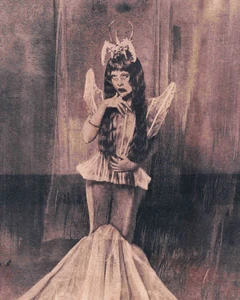 Melanie Martinez wearing a sculptural headpiece, translucent wings, and a mermaid gown in a moody textured editorial portrait.
