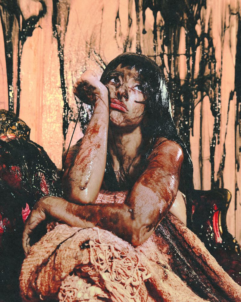 Melanie Martinez smeared in dark viscous liquid resting her chin on her hand for 1883 Magazine.
