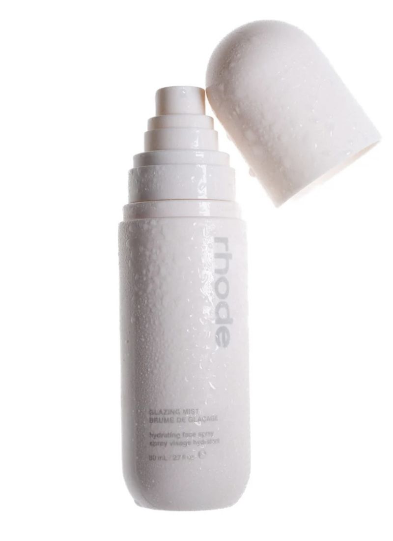 Close-up studio shot of a white bottle of Rhode Glazing Mist with its cap off against a plain white background, showcasing beauty product.