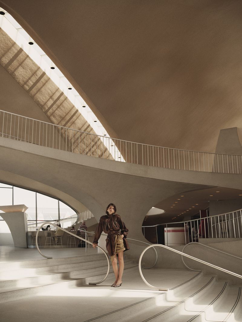 Model Georgia Fowler standing on a sweeping modernist concrete staircase with curved white railings in an editorial portrait.