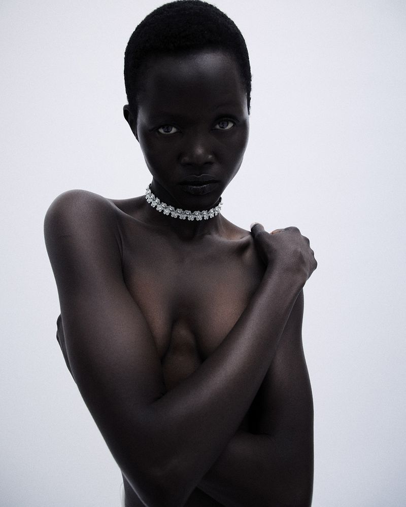 Anyiel Majok posing with crossed arms while wearing a sparkling choker necklace against a pale grey background.
