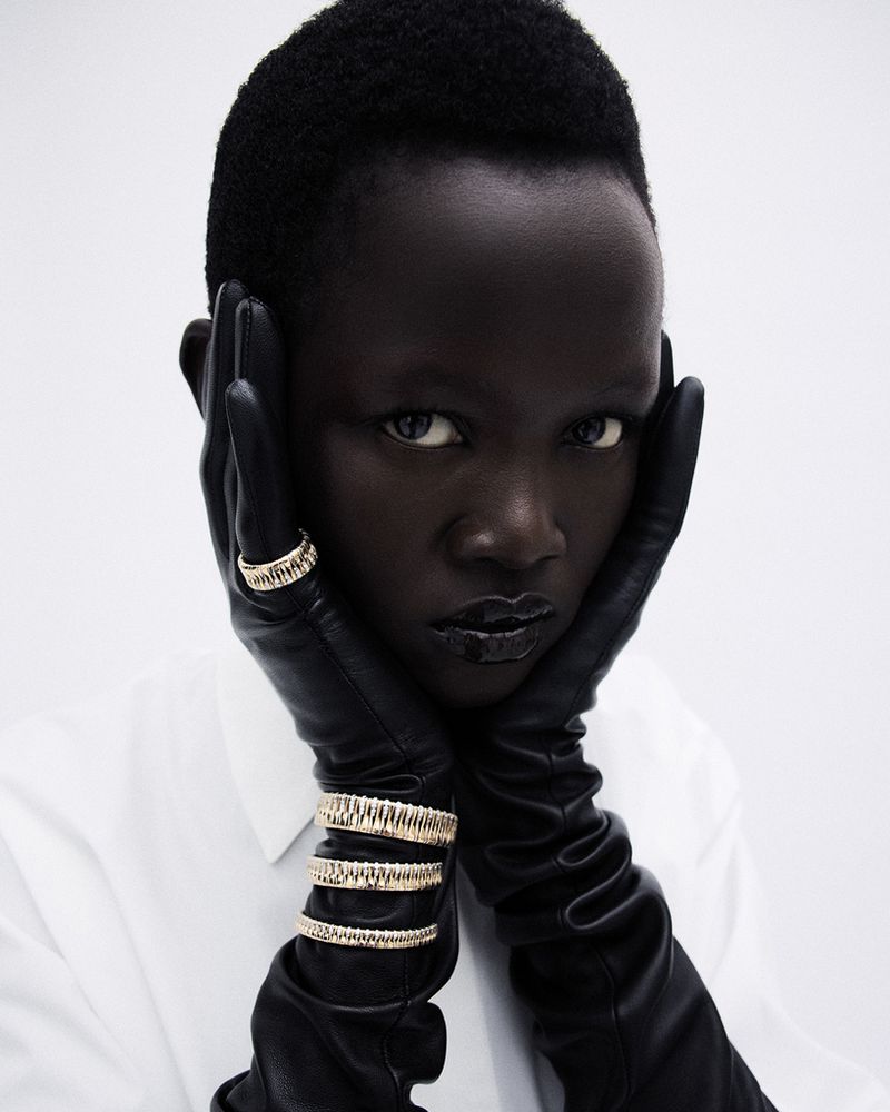 Model Anyiel Majok wearing black leather gloves and gold rings against a white background for Amica project Oro Puro.