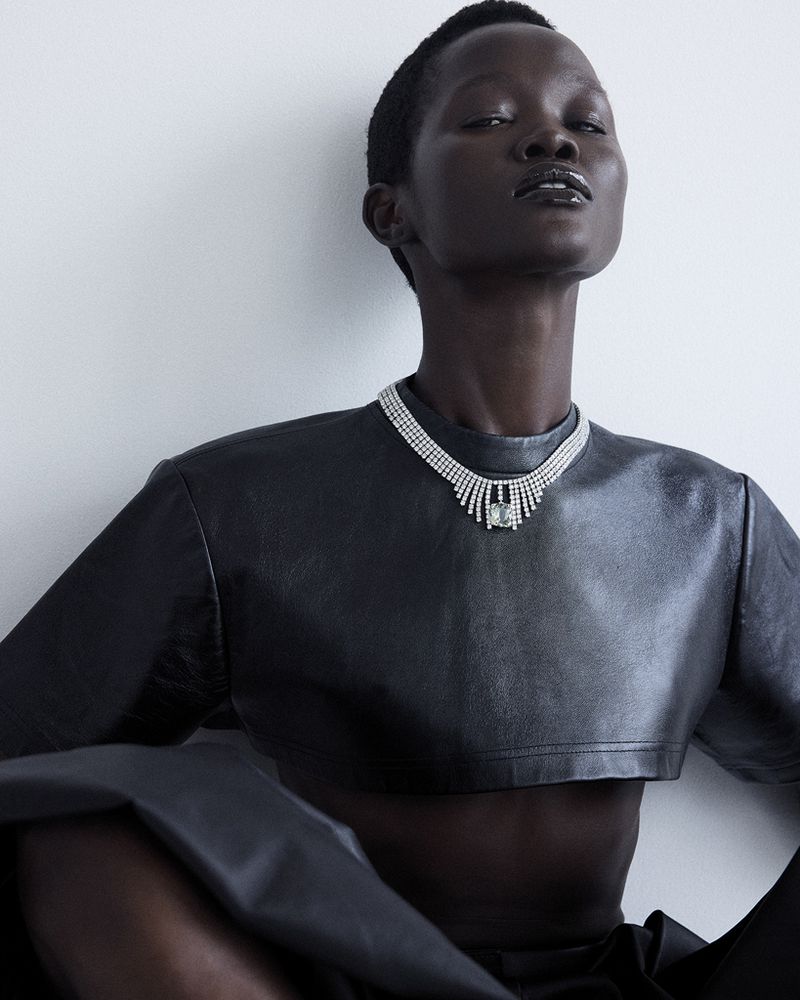 Model Anyiel Majok wearing a cropped black leather top and an ornate silver gemstone necklace against a clean studio background.