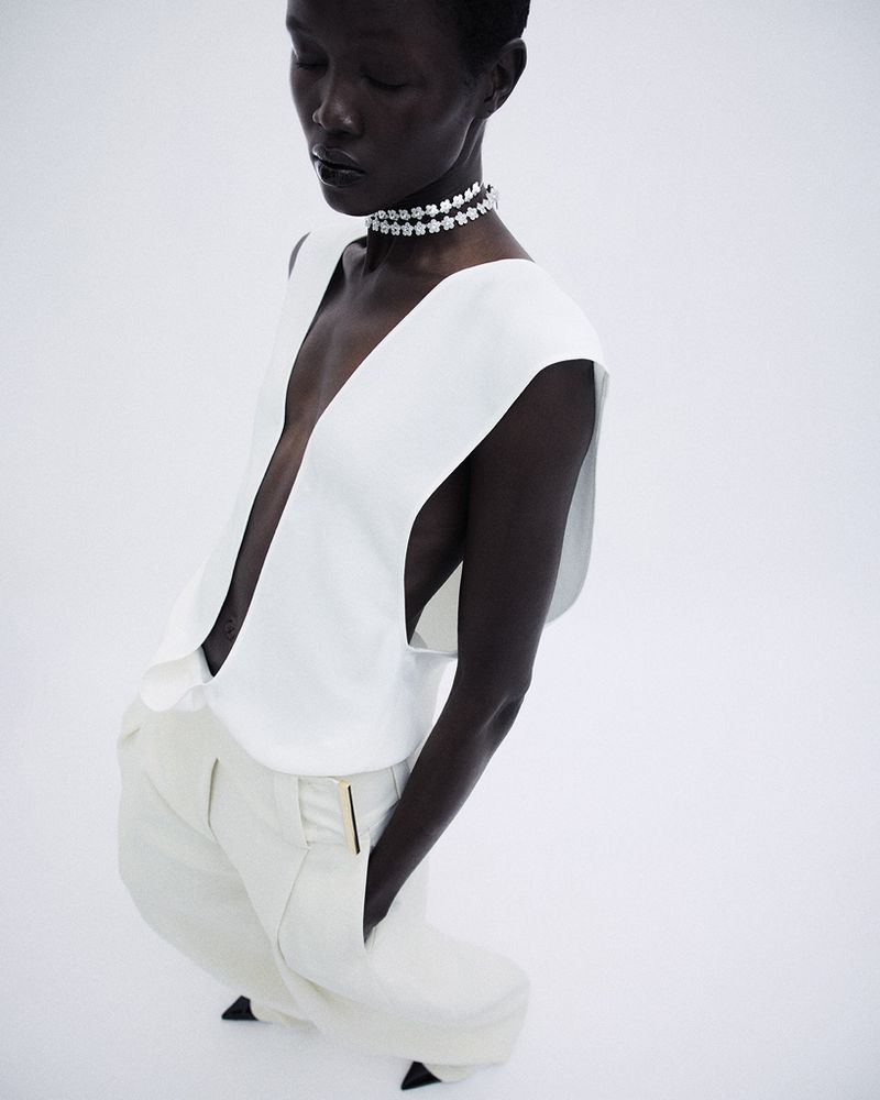 Model Anyiel Majok in a plunging white vest and cream trousers posing on a white seamless background.