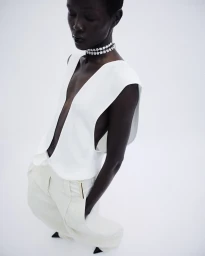Model Anyiel Majok in a plunging white vest and cream trousers posing on a white seamless background.
