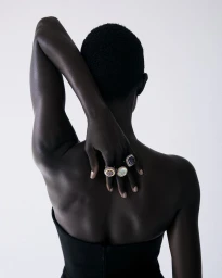 Model Anyiel Majok viewed from behind displaying gemstone cocktail rings with hand on spine against a white seamless backdrop.